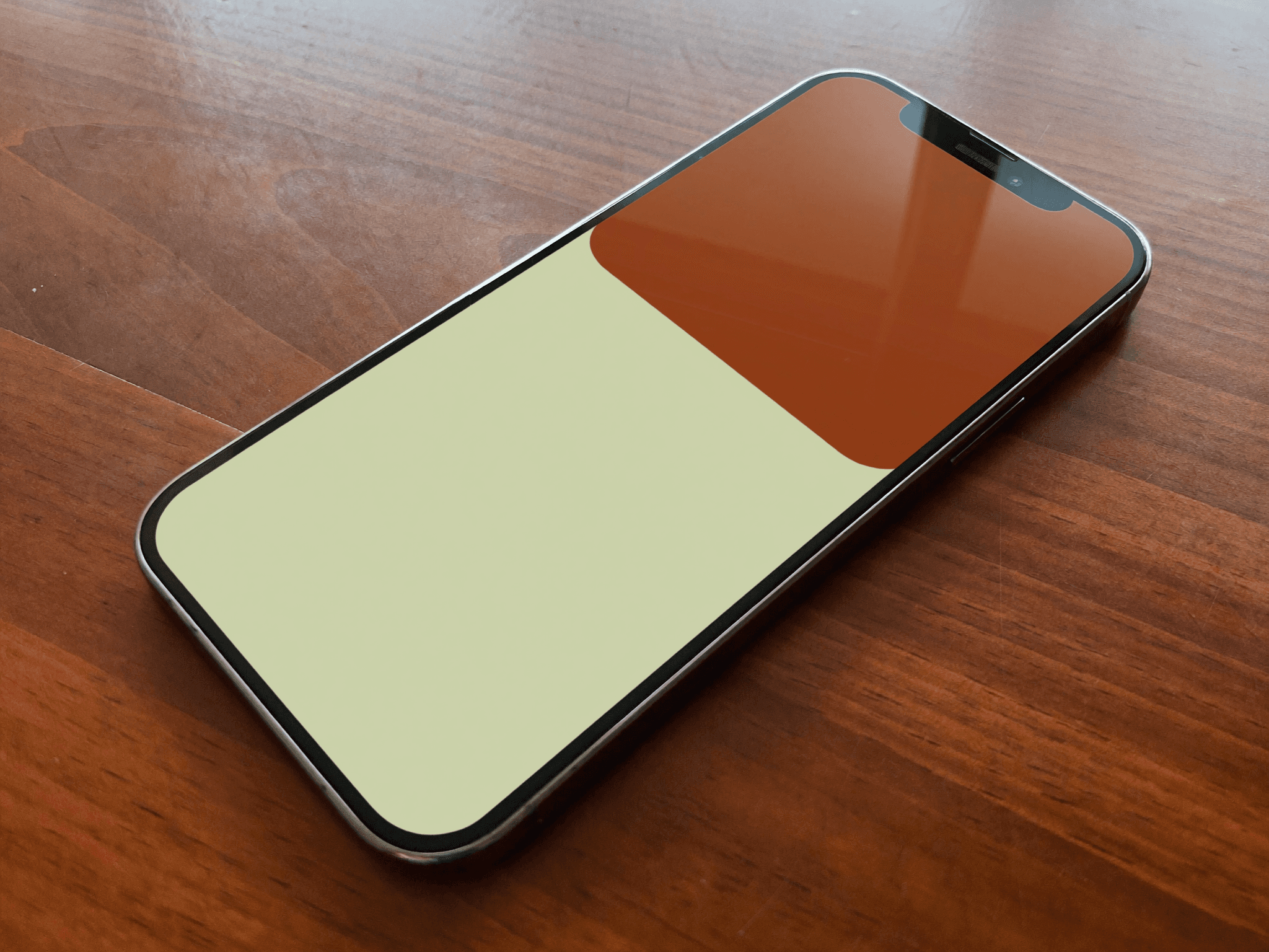 An iPhone on a warm hardwood surface showing an abstract Apple Wallet card in cream and terracotta.